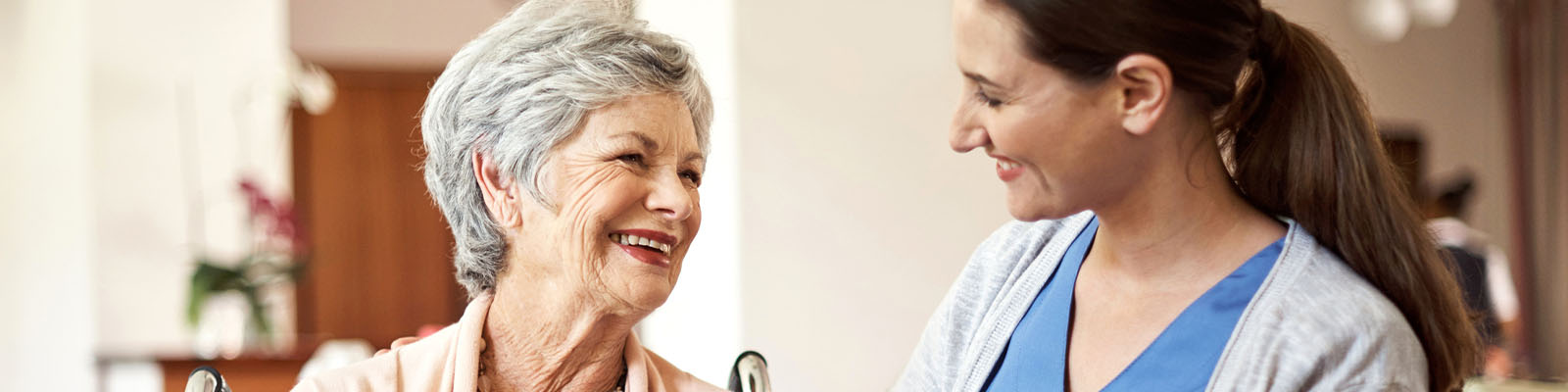 A senior woman sitting in a wheelchair looking at her female nursing assistant