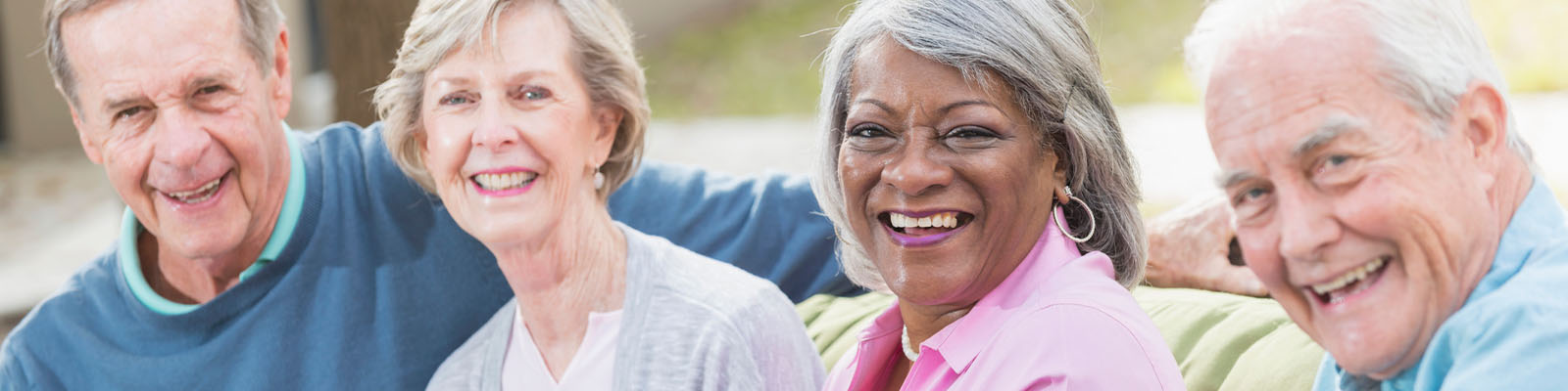 A group of senior men and women sitting on an outdoor couch smiling