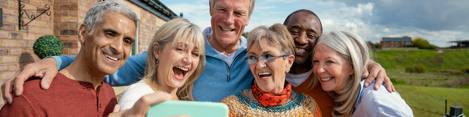 A close-up of six elderly adults outside, smiling for a selfie.
