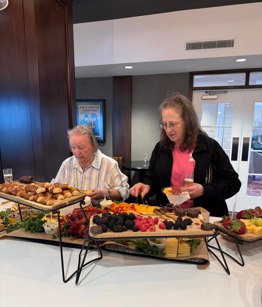 Residents enjoy a charcuterie board featuring fresh fruit, cheeses, meats, and appetizers during a social event.