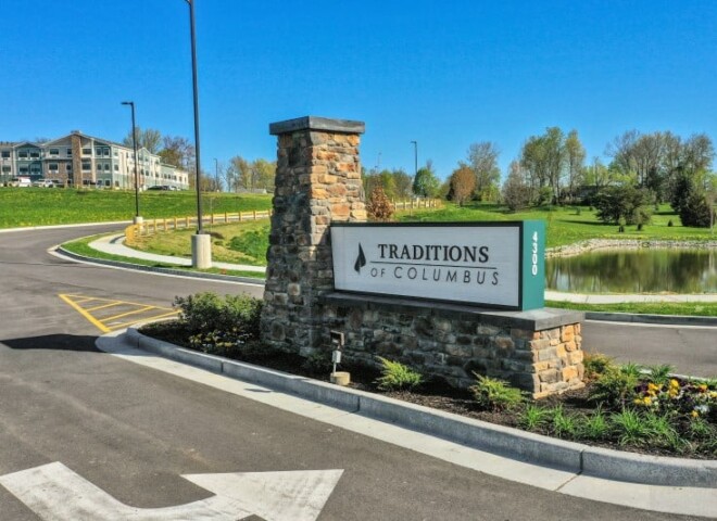 a community signage in front of a pond that says Traditions of Columbus with the Traditions community building in background